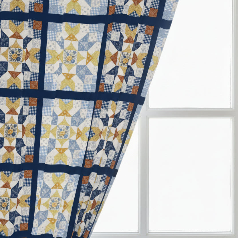 A close-up of a quilted fabric patterned printed panel featuring a geometric star and block pattern in navy blue, cream, yellow, and light blue, with a diagonal fold on a plain white background.