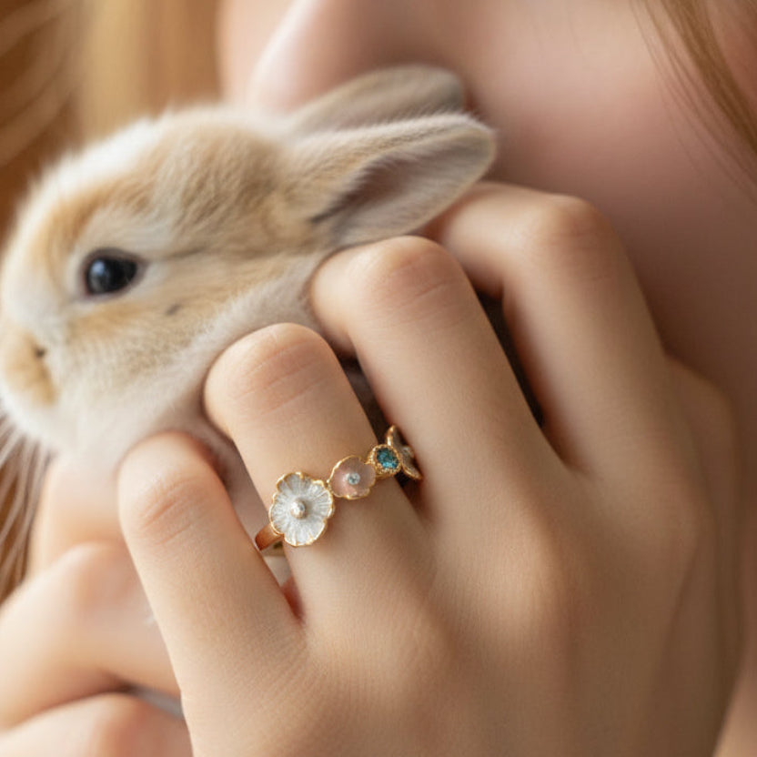 Person holding a small rabbit with a close-up of a hand wearing a ring featuring a floral design.