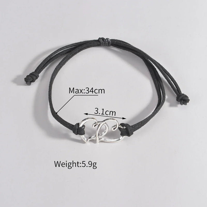 Black cord ankle bracelet with silver heart-shaped charm on a light gray background w measurements