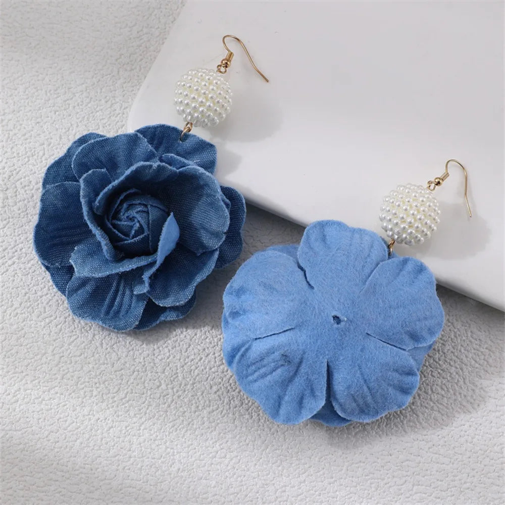 Blue flower-shaped earrings on a textured surface with a white dish in the background.