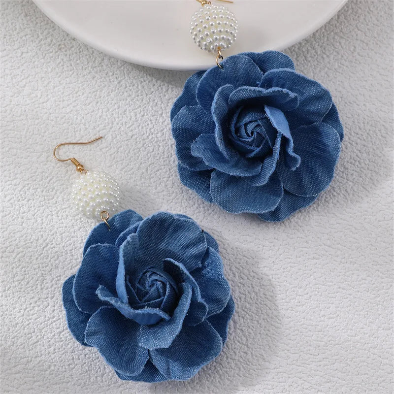 Blue flower earrings on a textured surface with a white plate in the background.