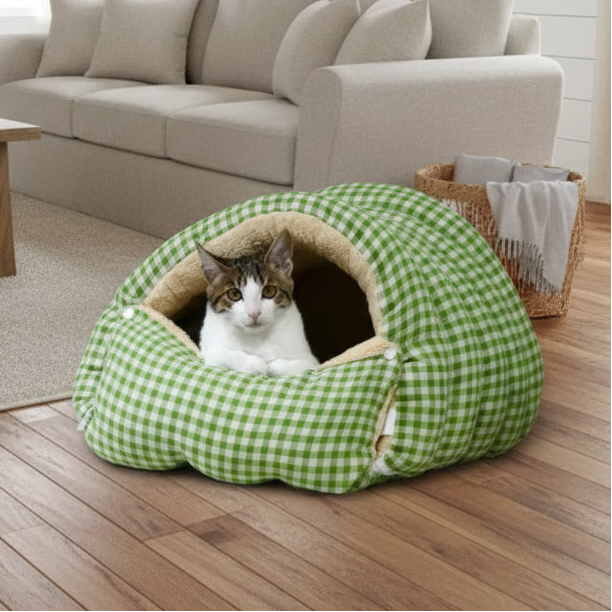 Cat lying inside a green checkered pet bed near a light-colored couch.