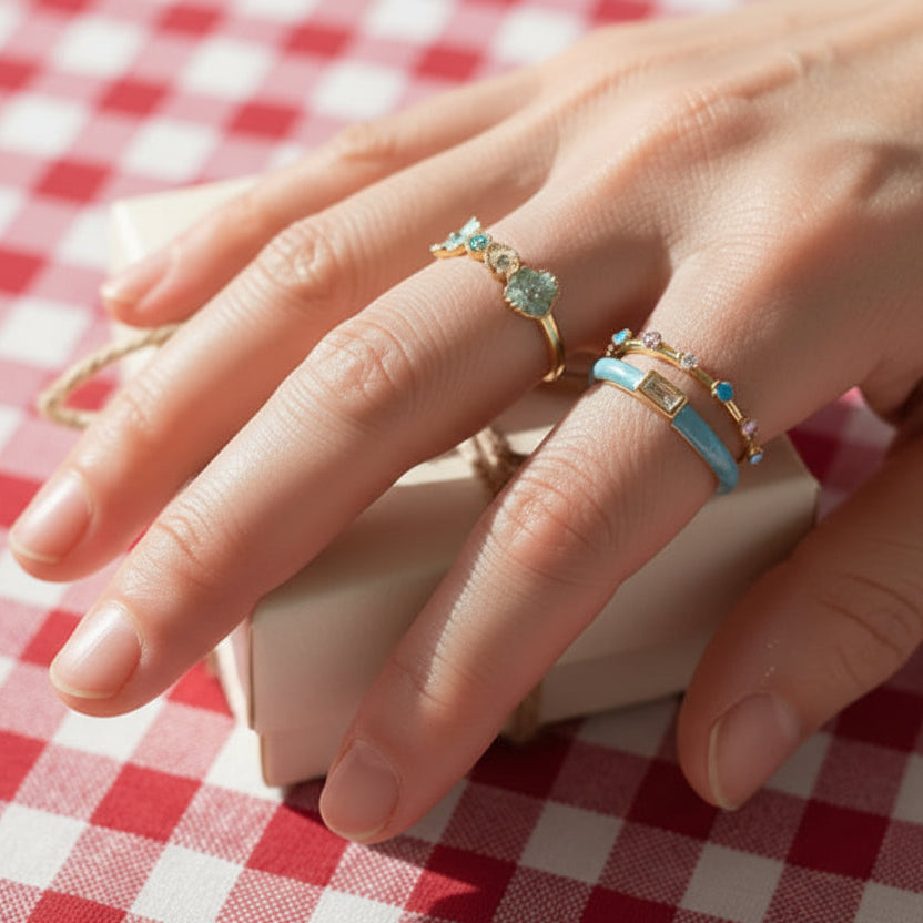 Close-up of a hand wearing multiple rings on a red and white checkered tablecloth.
