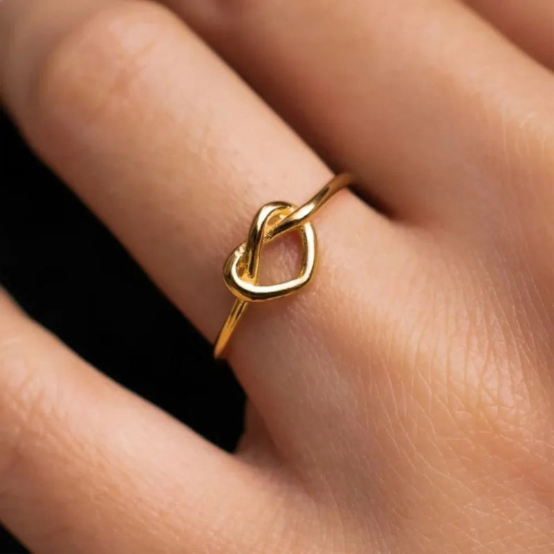 Gold ring with a unique design on a finger against a neutral background