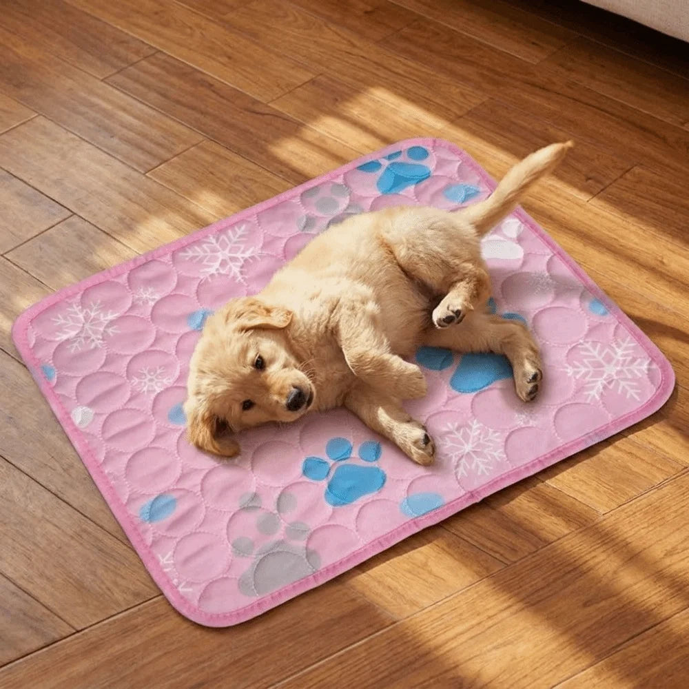 A golden retriever puppy lies on a pink cooling mat with paw prints and snowflake patterns on a wooden floor.