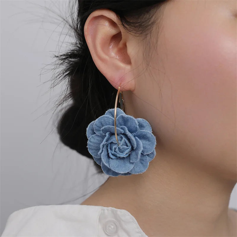 Close-up of a person wearing a blue floral earring against a neutral background
