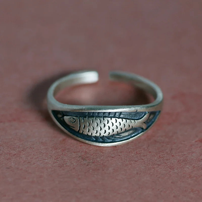 Silver fish-shaped ring on a textured brown background