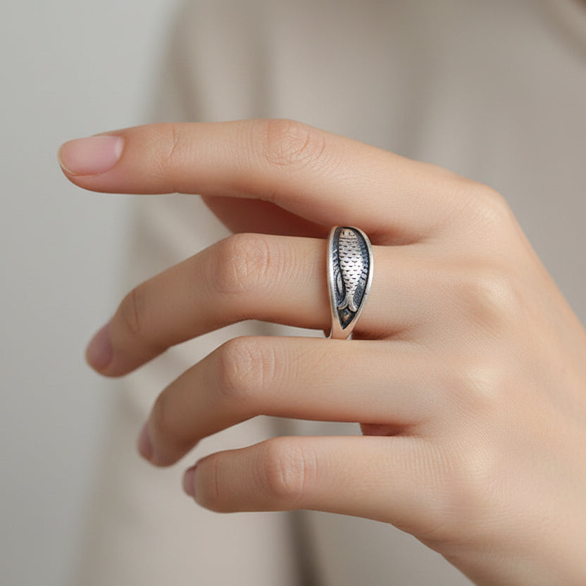 Hand wearing a silver ring with intricate design on a neutral background