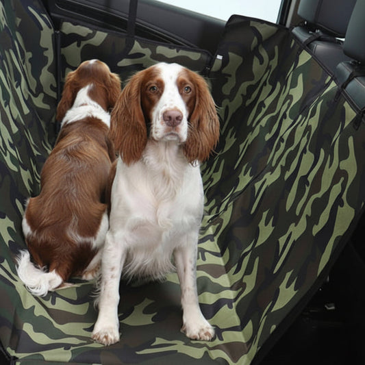 A dog car seat cover with a green and black camouflage pattern is shown installed inside a car, with two dogs seated on it.