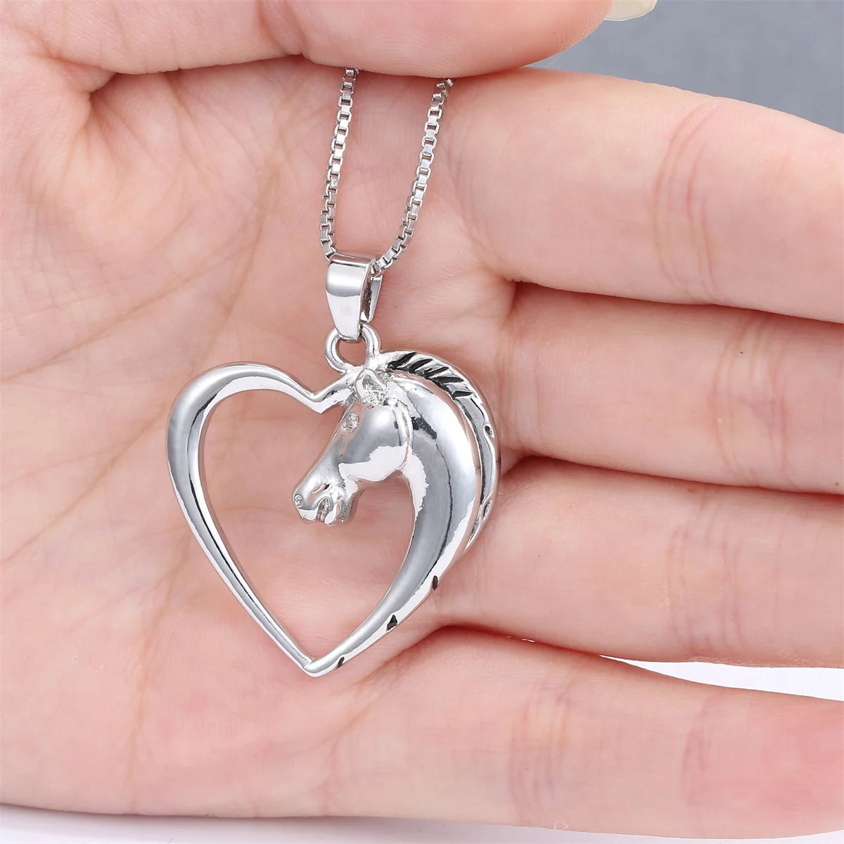 Silver necklace with a heart-shaped pendant featuring a horse design held in a hand.