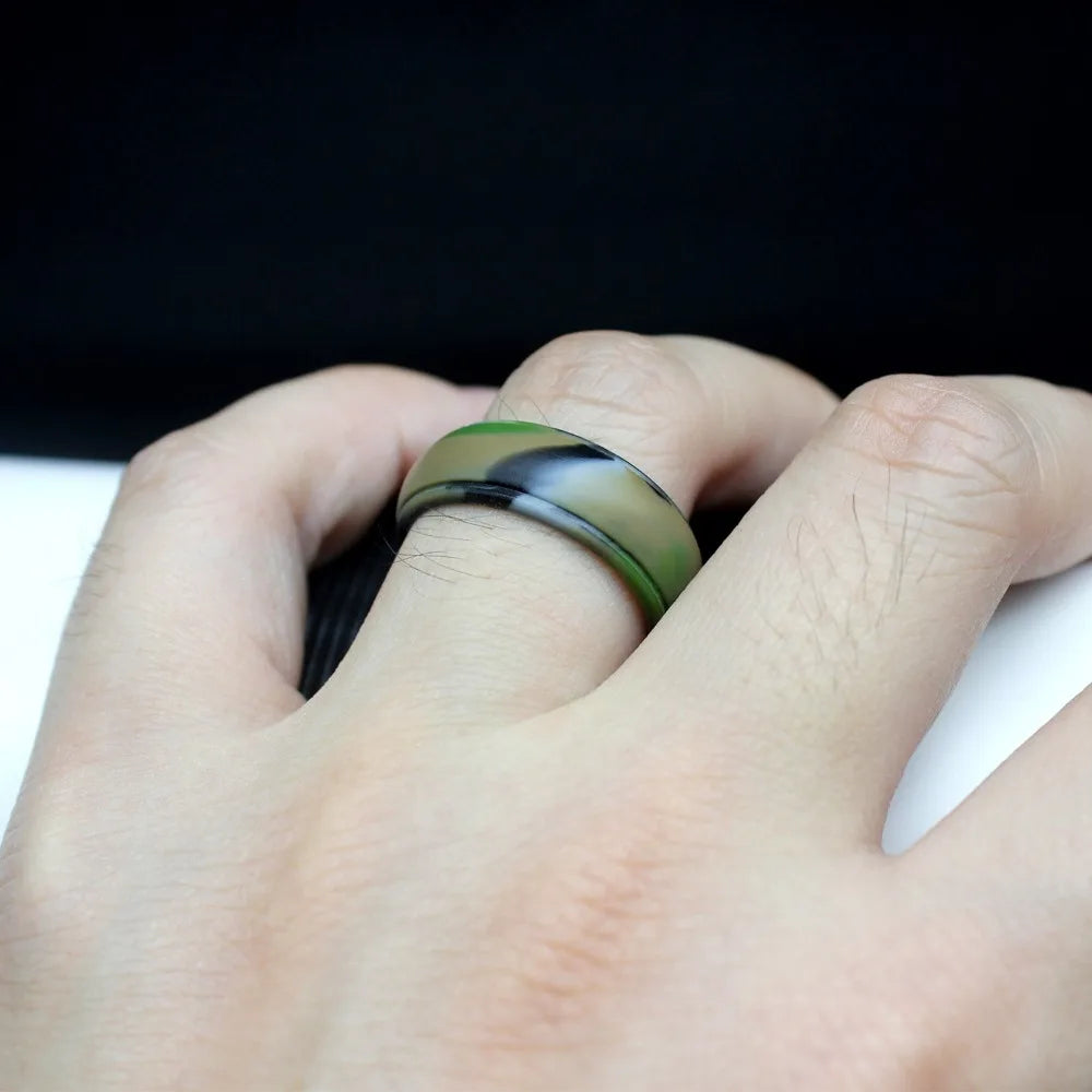 Hand wearing a ring with a black and green band on a dark background