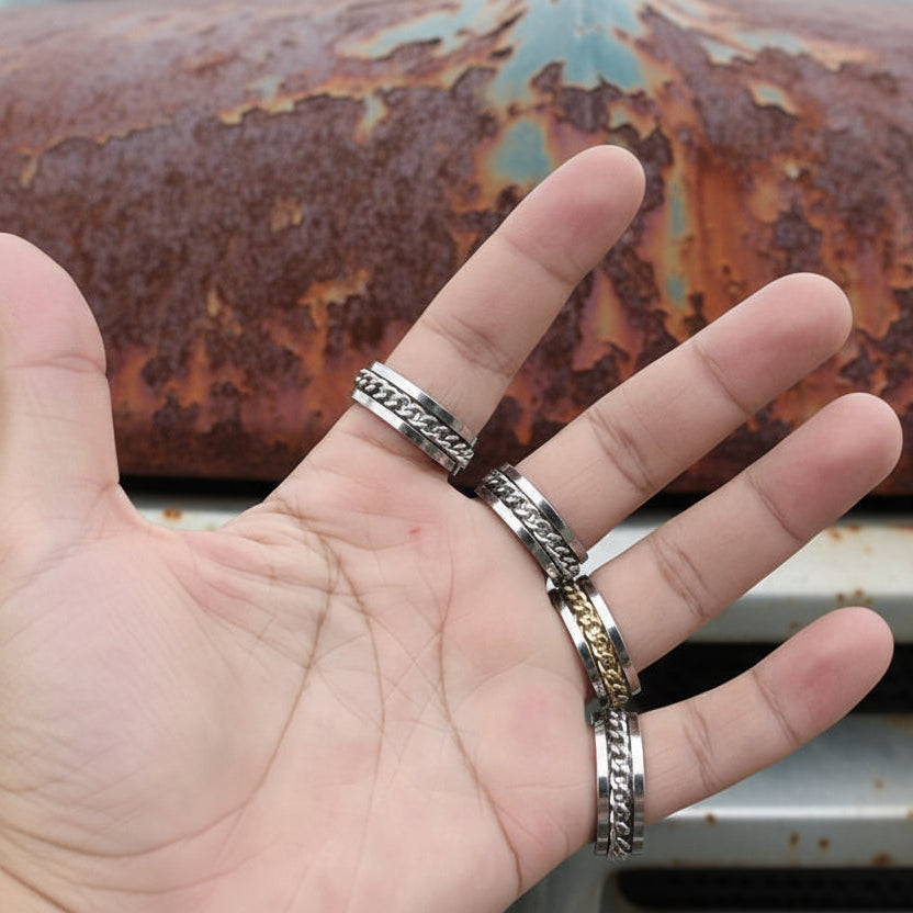 Hand wearing four metallic rings with different designs on a white background