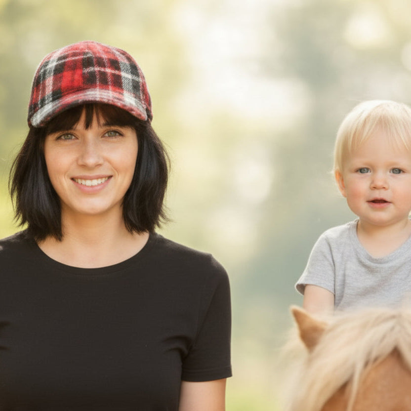 Woman wearing a plaid cap and black shirt standing next to a child on a pony