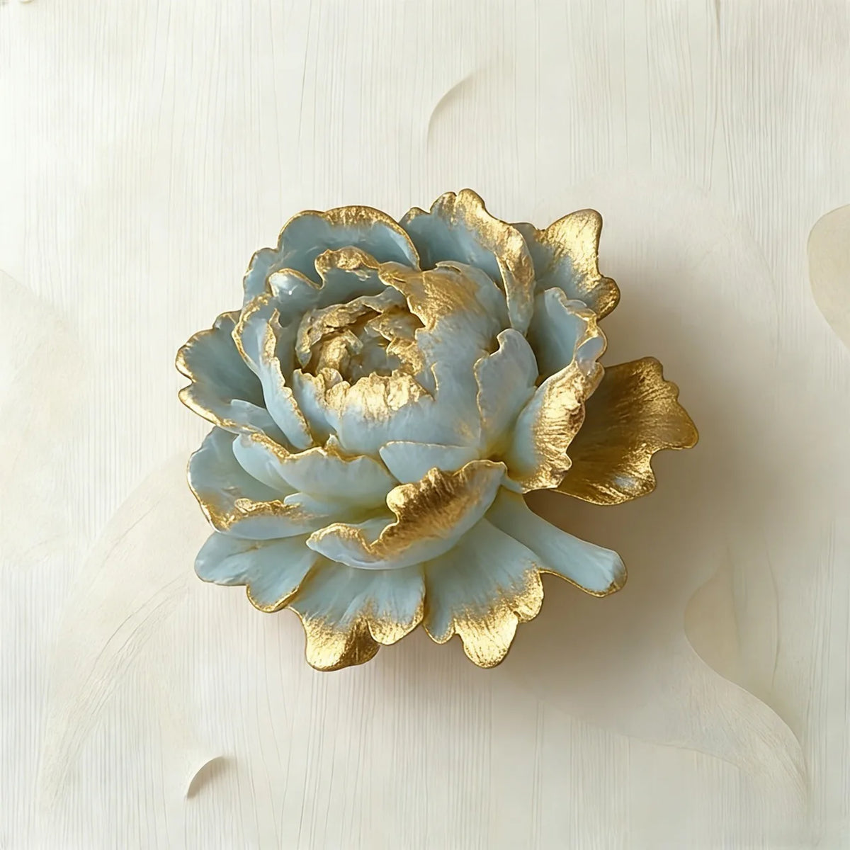 A decorative artificial flower with pale blue petals and metallic gold edges, photographed on a soft off-white textured background.