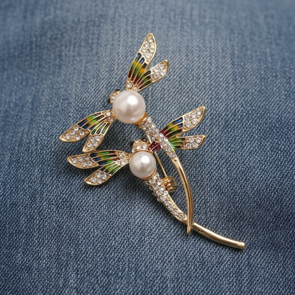 brooch of two dragonflies lying on blue denim fabric