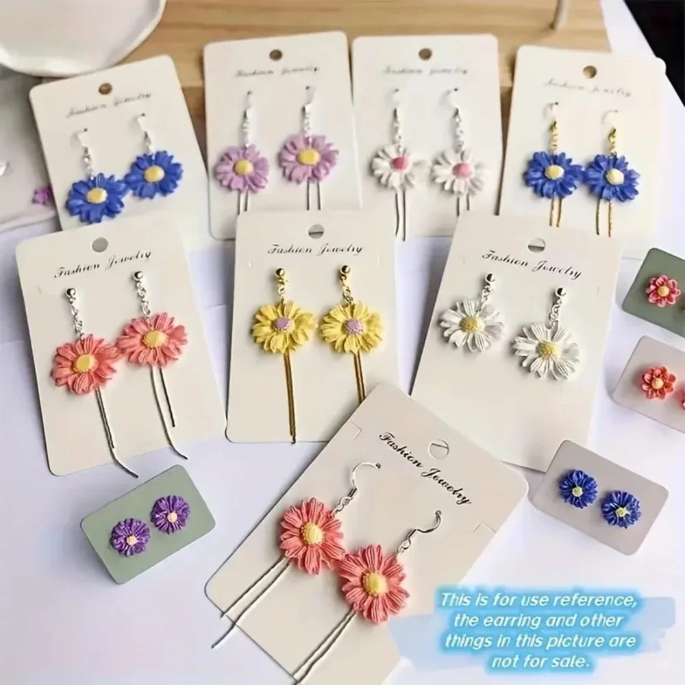 A collection of colorful flower-shaped dangle earrings displayed on white jewelry cards, with some matching earrings shown on small square cards. The flowers feature pink, yellow, blue, purple, and white petals with gold and silver metal findings.