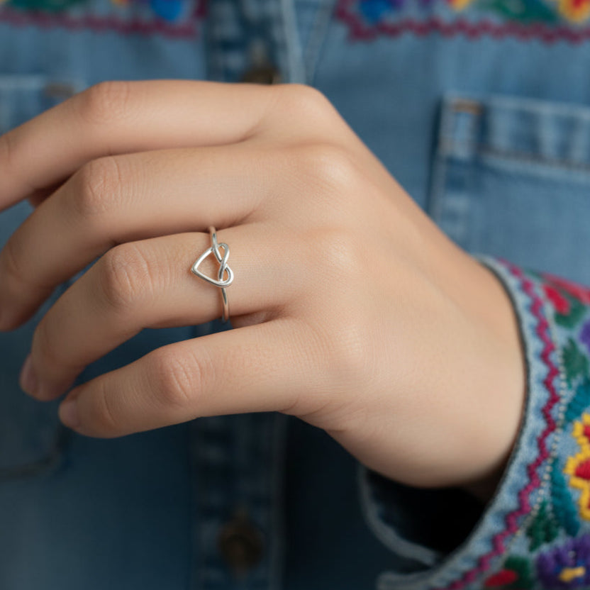 Hand wearing a silver ring with a heart design against a colorful denim background