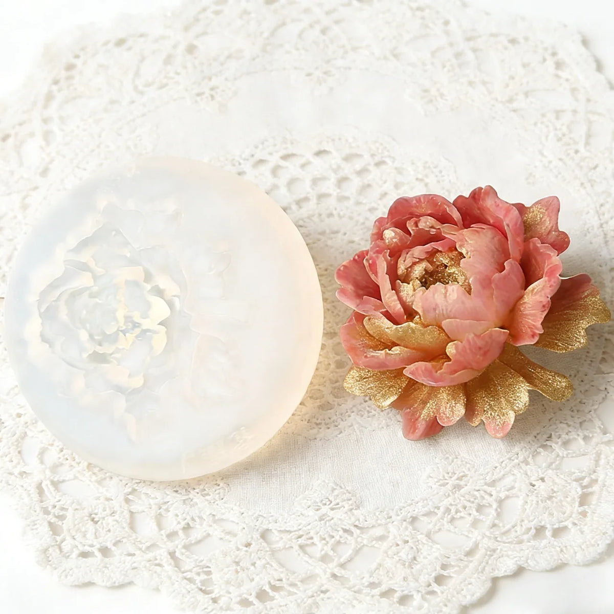 Decorative pink flower with gold accents on a white lace doily