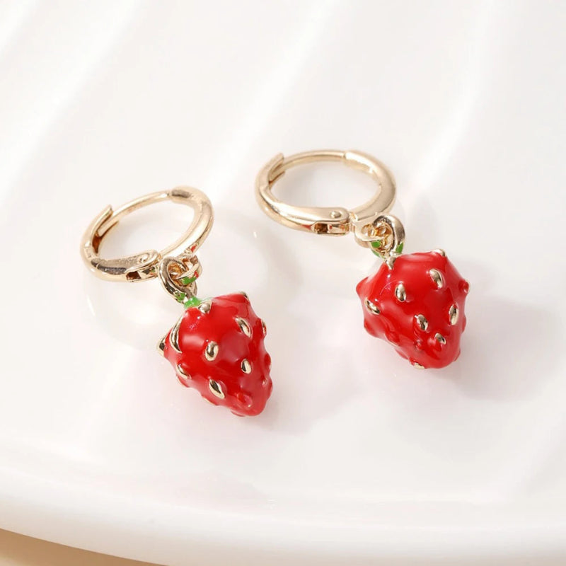 Gold hoop earrings with red strawberry-shaped charms on a white background