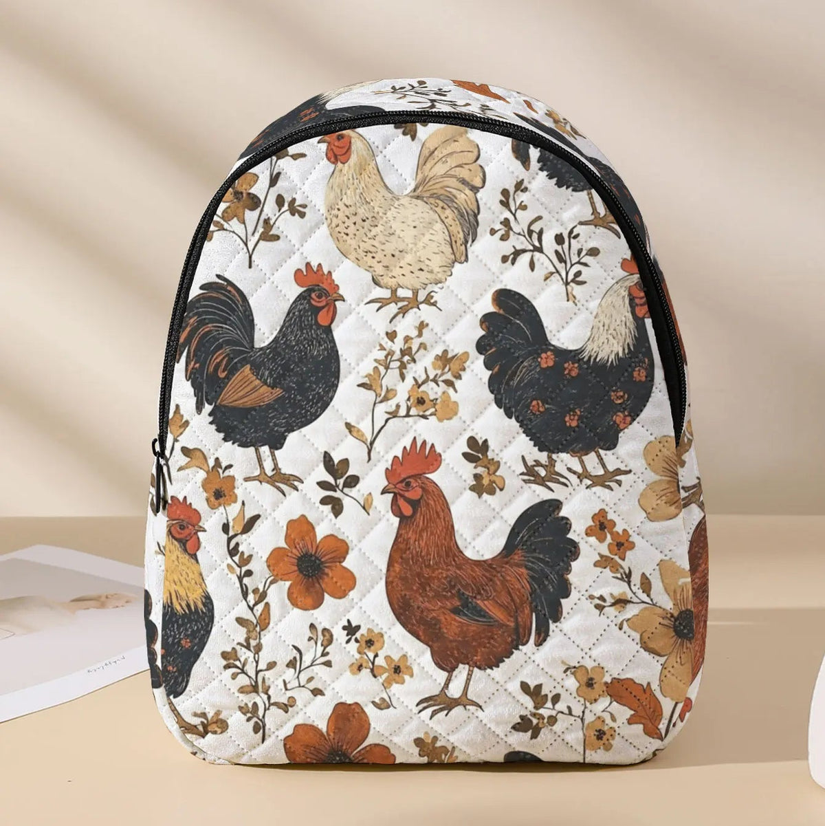 A quilted backpack featuring a vintage-style print of various chickens and floral motifs on a cream background, with black trim and zippers, set against a warm beige background.